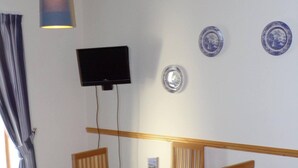 A dining area with a wooden table and chairs, a television mounted on the wall, and decorative plates on the wall.