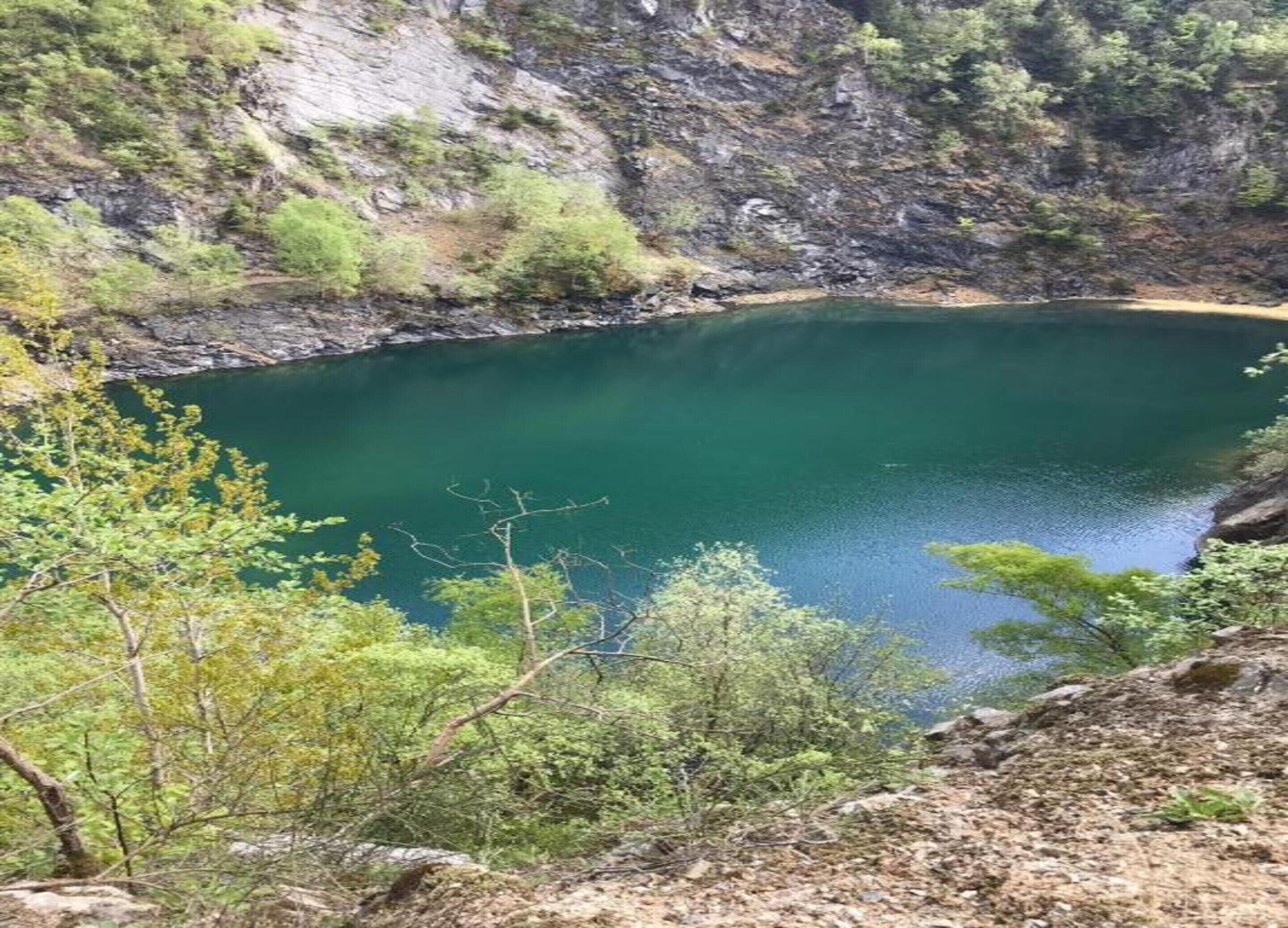 A natural landscape with a clear lake surrounded by rocky cliffs and sparse vegetation.