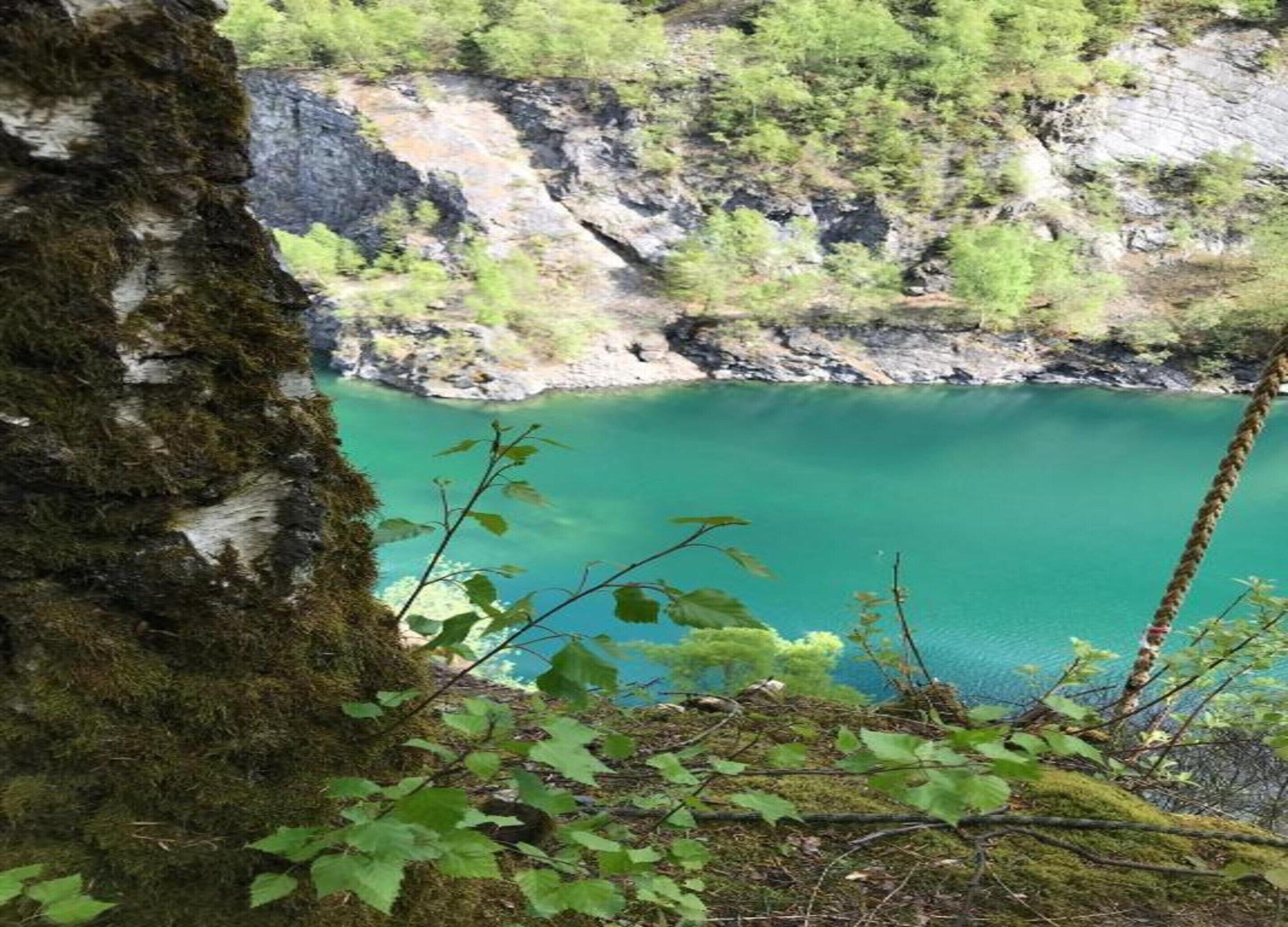 A natural landscape with a clear turquoise lake surrounded by rocky cliffs and sparse vegetation.
