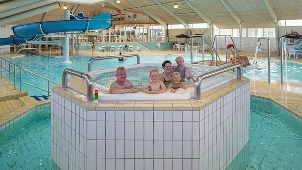 Une piscine intérieure dotée d’un espace avec bain à remous, de sièges et d’un toboggan.