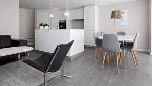 Une cuisine moderne avec des meubles blancs, un coin repas doté d’une table ronde et de chaises grises, et un canapé en cuir noir.