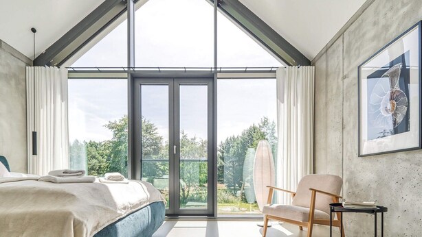 Un dormitorio moderno con un tragaluz grande, una cama, una silla y una mesa.