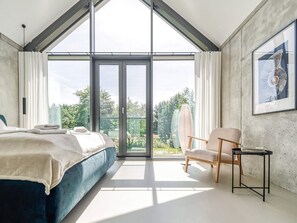 A modern bedroom with a large skylight, a bed, a chair, and a table. - Ferienhaus in Fuhlendorf am Boddenhafen (Fuhlendorf)