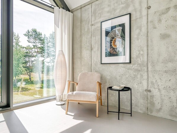 A modern room with a large window, a chair, a small table, and a framed artwork on the wall. - Ferienhaus in Fuhlendorf am Boddenhafen (Fuhlendorf)