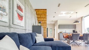 Una sala de estar moderna con un sofá modular, un comedor con mesa y sillas, y una cocina al fondo.
