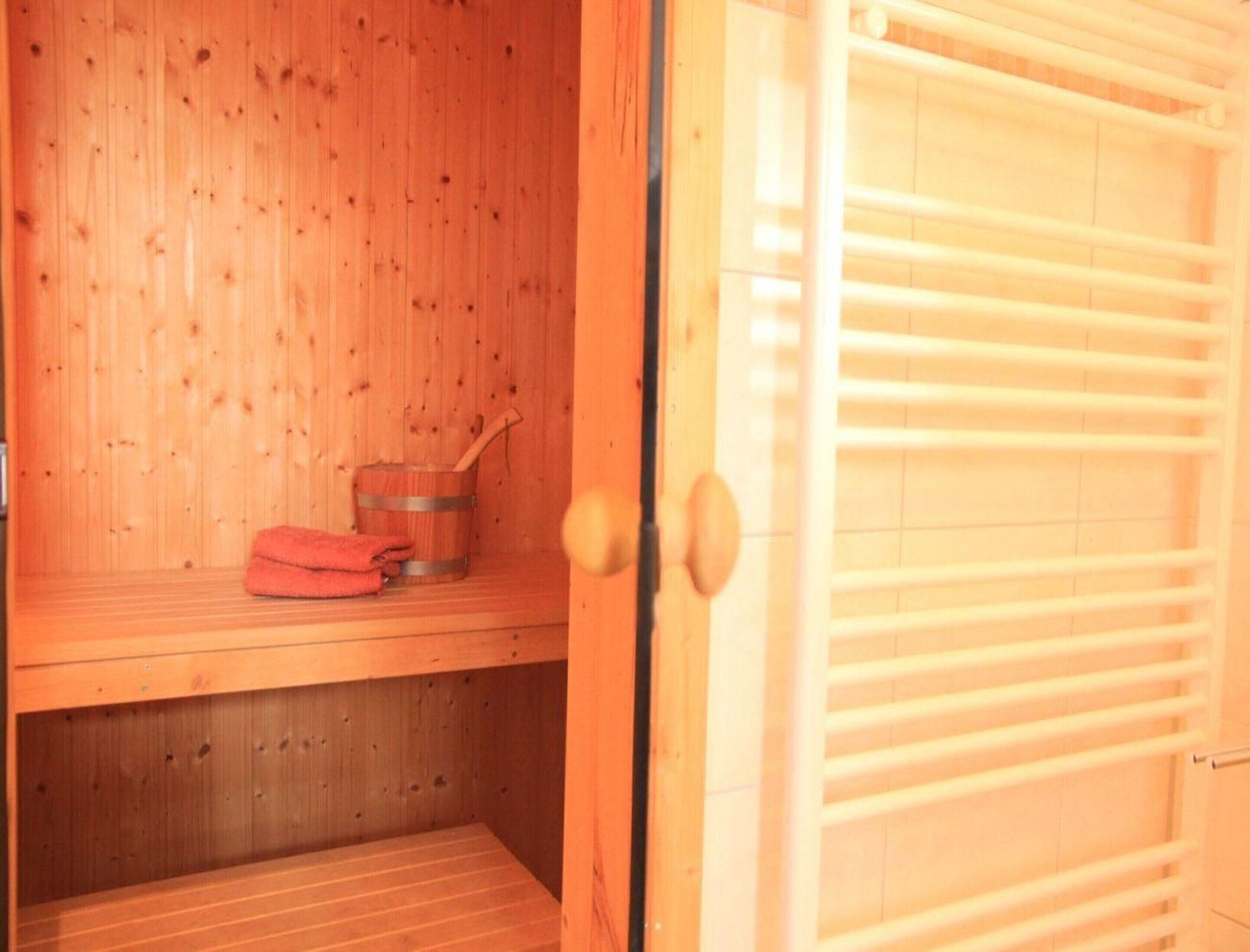 Een houten sauna met een bankje, een emmer en een handdoek.