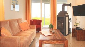 A living room with a sofa, armchair, wooden coffee table, and a fireplace. - Ferienwohnung im Ferienpark Mueritz (Rechlin)