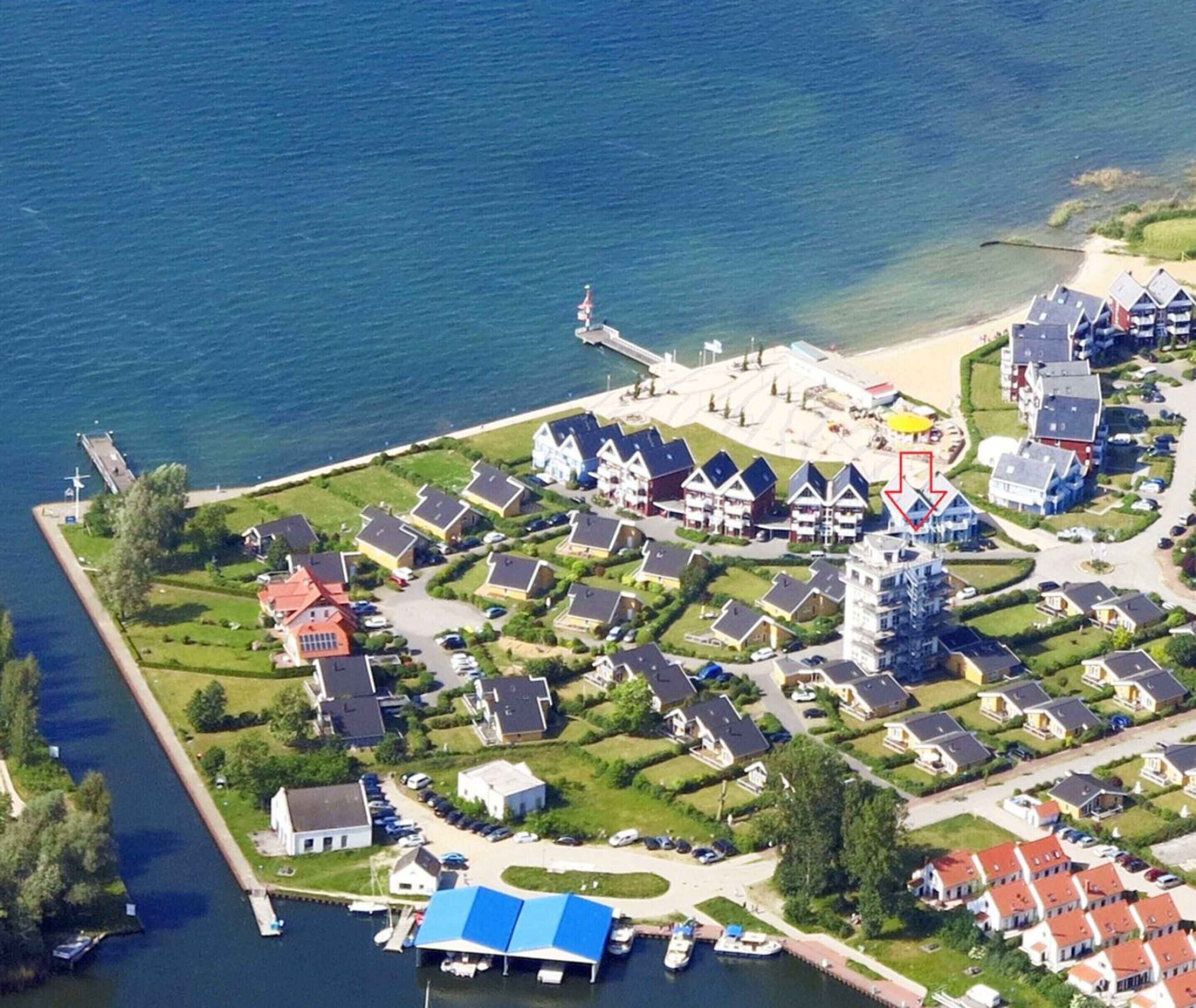 An aerial view of a coastal residential area with houses, a marina, and a pier.