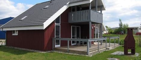 A red building with a grey roof, a balcony, and a small porch area.