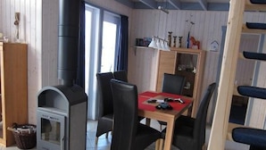 Una habitación acogedora con una estufa de leña, una mesa de comedor con sillas y una estantería.