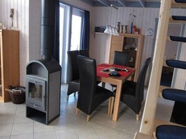 Una habitación acogedora con una estufa de leña, una mesa de comedor con sillas y una estantería.