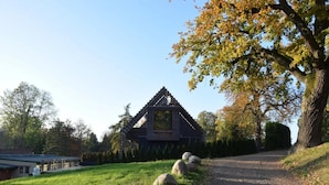 A rustic cabin with a sloped roof, surrounded by a grassy area with large rocks and trees. - Chalet in Wendorf (Kuhlen-Wendorf)