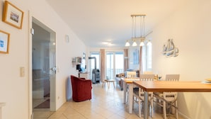 A spacious living area with a dining table, red chair, and a kitchen area in the background. - Exquisite Ferienwohnung in Rechlin (Rechlin)