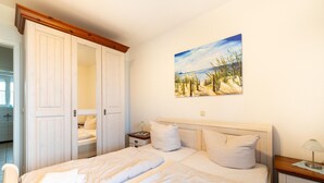 A bedroom with a bed, a nightstand, a lamp, and a painting of a beach scene. - Exquisite Ferienwohnung in Rechlin (Rechlin)