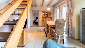 Een houten trap die leidt naar een eetgedeelte met rieten stoelen en een tafel.