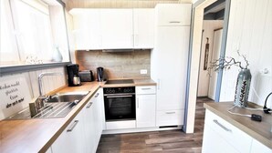Een kleine keuken met witte kastjes, een ingebouwde oven, een koffiezetapparaat en een spoelbak.