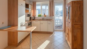 A modern kitchen with wooden cabinets, a central island, and a view of a balcony. - Exklusives Appartement in Rechlin (Rechlin)