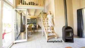 A spacious room with a loft area, a black wood-burning stove, and a dining area with a table and chairs. - Skandinavisches Ferienhaus in Mirow (Mirow)