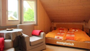 A cozy attic bedroom with a checkered chair, a small round table, and a bed with an orange bedspread. - Skandinavisches Ferienhaus in Mirow (Mirow)