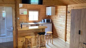 A compact wooden cabin with a kitchenette, a sink, a microwave, and two stools. - Cottage in Dziwnowek Near Baltic Beach (Dziwnów)
