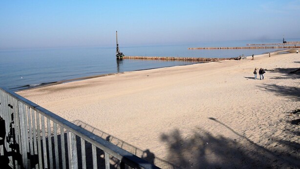 A beach with a pier extending into the water, a sandy shore, and a few people walking. - Cottage in Dziwnowek Near Baltic Beach (Dziwnów)