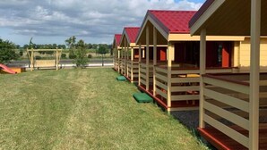 A row of wooden cabins with red roofs, each with a porch and a small step leading up to the entrance. - Cottage in Dziwnowek Near Baltic Beach (Dziwnów)