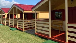 A row of single-story cabins with red roofs and white walls, each with a porch and a bench. - Cottage in Dziwnowek Near Baltic Beach (Dziwnów)