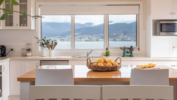 Cocina moderna con un amplio ventanal, una isla de madera, armarios blancos y vistas a un paisaje nevado.