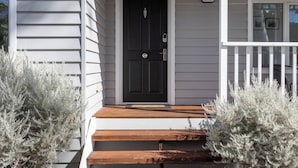 Una casa con puerta principal oscura, revestimiento blanco y porche delantero de madera.