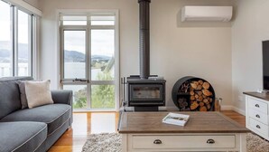 Una sala de estar moderna con chimenea, un sofá gris, una mesa de centro y vistas a un lago.