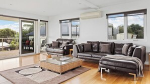 A spacious living room with a large leather sofa, a glass coffee table, and a view of the outdoors through large windows.