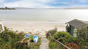 A beach view with a pathway leading to a small building, surrounded by greenery and a clear sky.