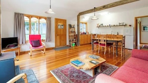 Een ruime woonkamer met een rode bank, een houten eettafel met stoelen, een televisie en een salontafel.