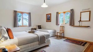 Een slaapkamer met twee bedden, een stoel, een bureau en een raam met gordijnen.