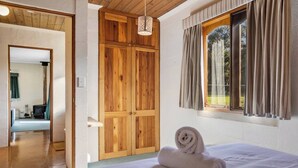 A bedroom with a wooden wardrobe, a bed with a rolled towel, a hanging light fixture, and a window with curtains. - The Clocktower Serene Stay at Herons Rise Vineyard (Kettering)