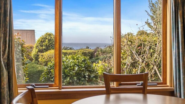 A room with a large window offering a view of a garden and the sea. - The Clocktower Serene Stay at Herons Rise Vineyard (Kettering)