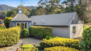 A small, single-story building with a sloped roof, surrounded by well-maintained hedges and flowering plants. - The Clocktower Serene Stay at Herons Rise Vineyard (Kettering)