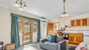 A cozy living room with a sofa, a small table, and a kitchen area with wooden cabinets and appliances. - The Clocktower Serene Stay at Herons Rise Vineyard (Kettering)