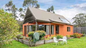Una casa de un piso con techo inclinado, ventanas amplias y un jardín con césped y mobiliario exterior.