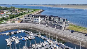 Un puerto deportivo con barcos amarrados, un edificio moderno con balcones, y una vista despejada del agua y la costa distante.