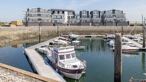 Un puerto deportivo con varias embarcaciones amarradas, un muelle de madera y edificios modernos de varios pisos al fondo.