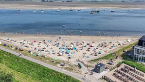 Una playa con numerosas sombrillas y gente, un sendero y un edificio con fachada de vidrio.