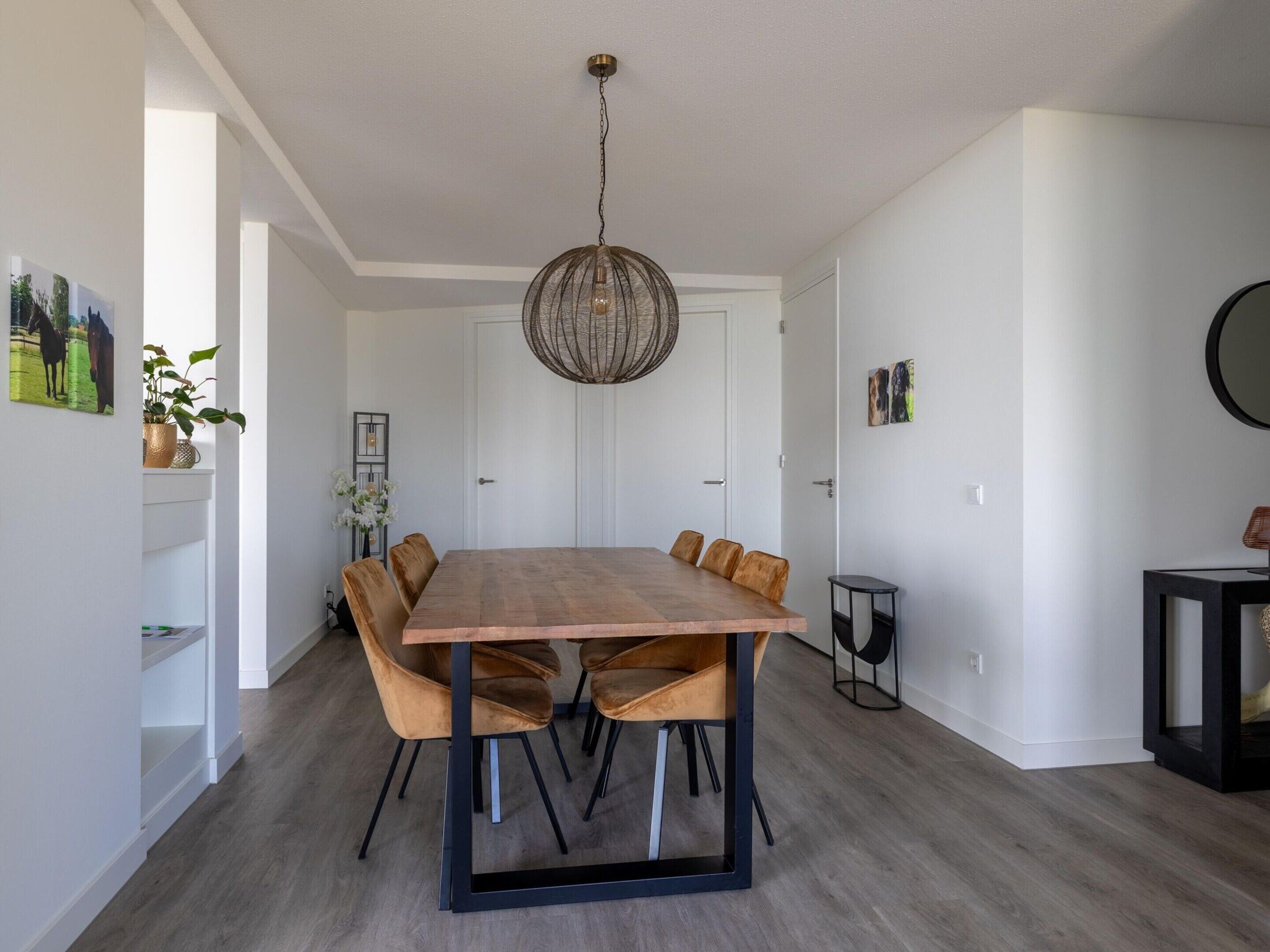 A modern dining area with a wooden table and leather chairs, a hanging light fixture, and white walls with artwork.