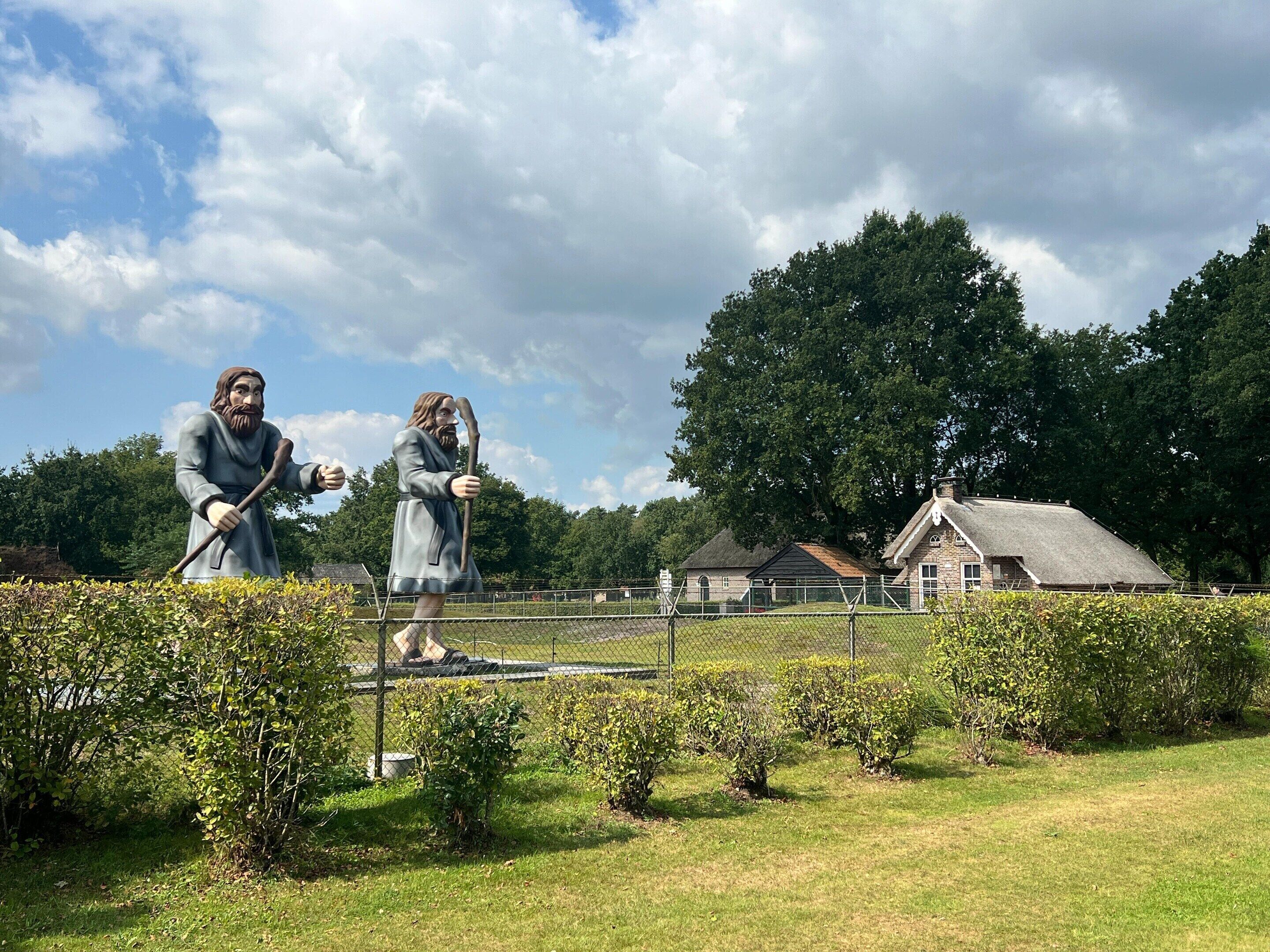 Two statues in a park with a house and trees in the background.