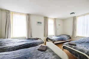 A room with three beds, each with a patterned bedspread and a pillow. There are curtains on the windows, and a picture hangs on the wall. - Cozy Holiday Home in a Lovely Environment (De Kiel)