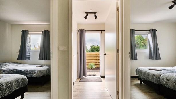 A hotel room with two beds, a wooden floor, and a view of the outdoors through a door. - Stay at This Beautiful Accommodation in De Kiel (De Kiel)