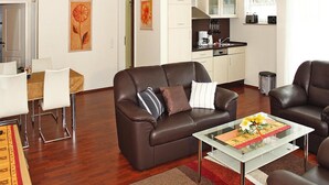 Un salon moderne avec un canapé en cuir marron, une table basse en verre et un coin repas comprenant une table et des chaises blanches.