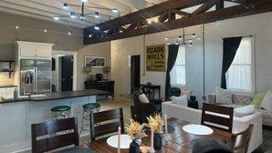 A spacious living area with a large wooden beam ceiling, a kitchen with a stainless steel refrigerator, and a dining area with a table set for four. - Historic 2 bedroom steps off downtown square (Mountain Home)