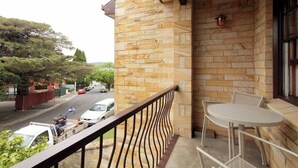 Ein Balkon mit Steinmauer, Blick auf eine Straße und ein Tisch mit Stühlen.