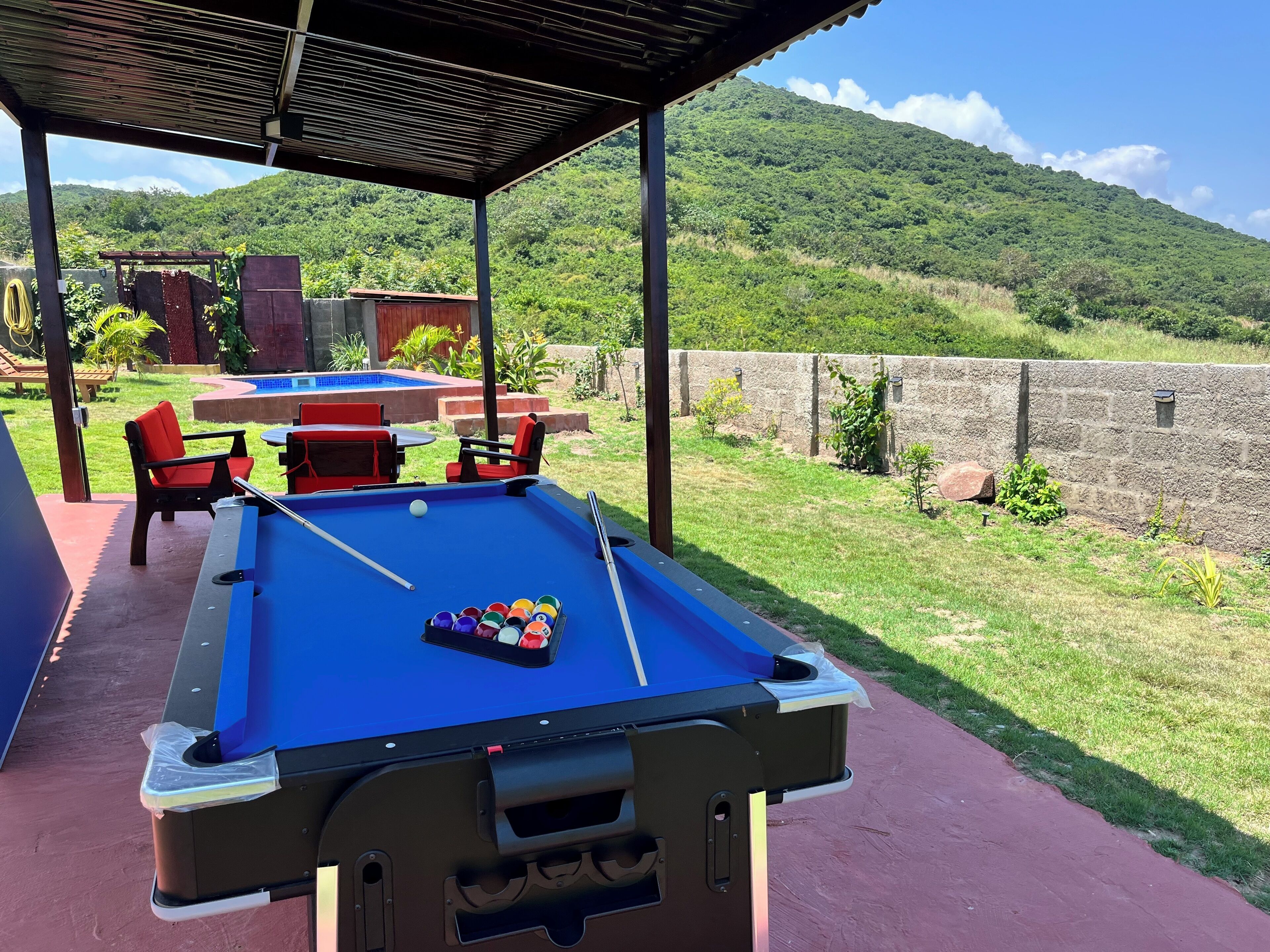 Une table de billard recouverte d’un drap bleu, avec un jeu de queues de billard, entourée de chaises rouges et noires.
